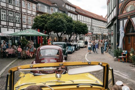 Blick aus einem gelben Oldtimer auf eine Oldtimer-Rallye in einer Fachwerk-Altstadt.