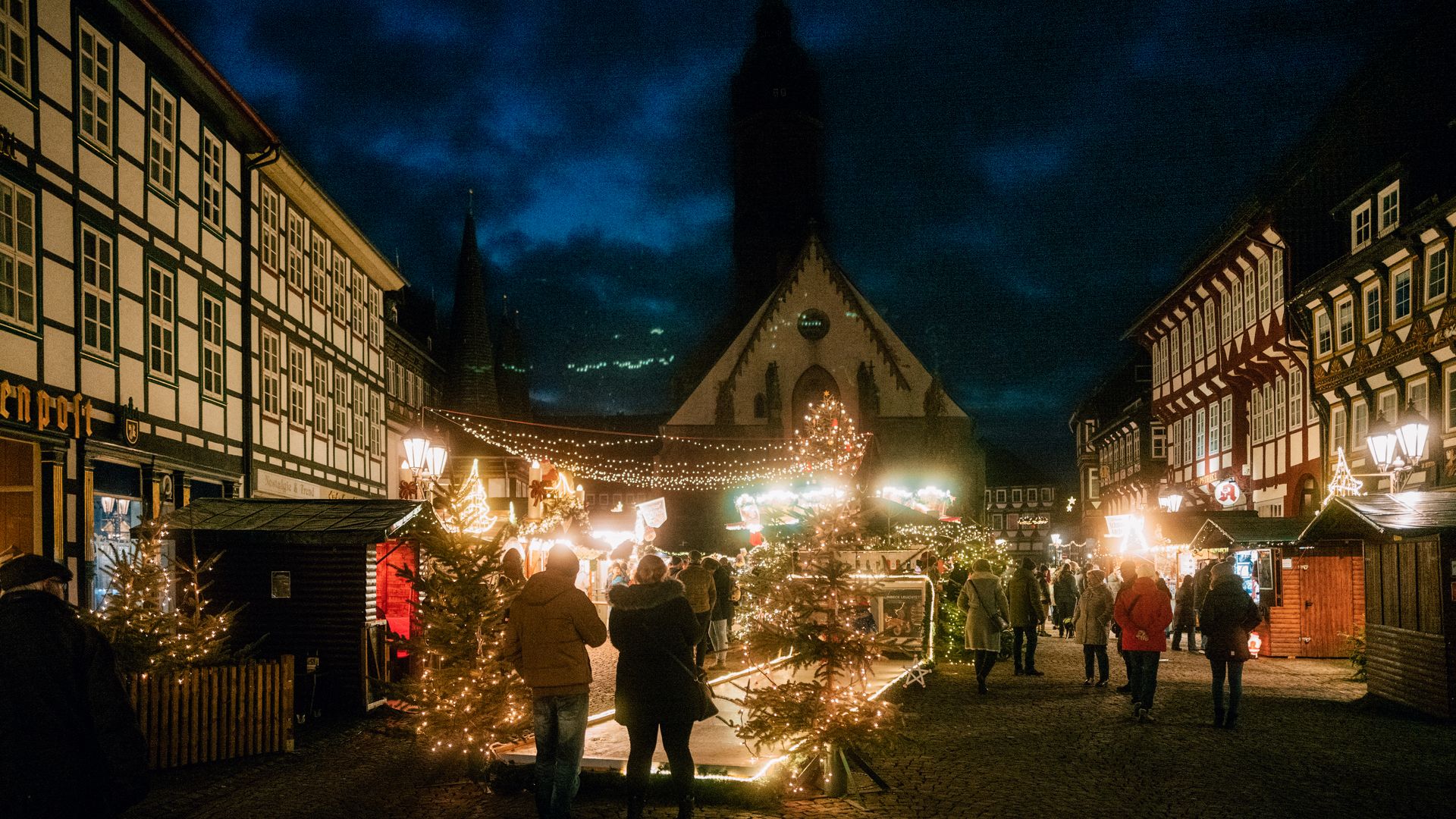Das beleuchtete Einbecker Weihnachtsdorf mit vielen Menschen auf dem Marktplatz im Dunkeln. Im Vordergrund die Stockbahn.