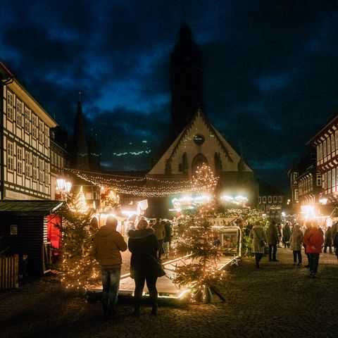 Das beleuchtete Einbecker Weihnachtsdorf mit vielen Menschen auf dem Marktplatz im Dunkeln. Im Vordergrund die Stockbahn.