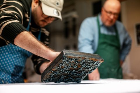 Zwei Männer arbeiten konzentriert beim Blaudruck mit einem verzierten Druckstempel auf Stoff.