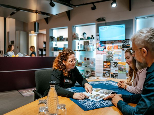 Tourist-Information Mitarbeiterin berät zwei Gäste an einem Tisch in der Tourist-Information Einbeck.