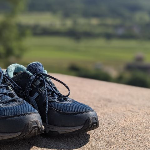 1 Paar Schuhe auf den Überresten einer Burgmauer. Im Hintergrund ist das Leinetal zu sehen.