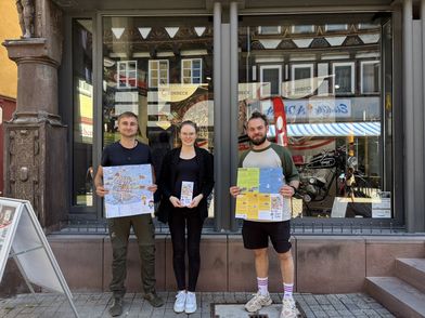 Drei Personen präsentieren vor dem Schaufenster der Tourist-Information Einbeck einen Kinderstadtplan.