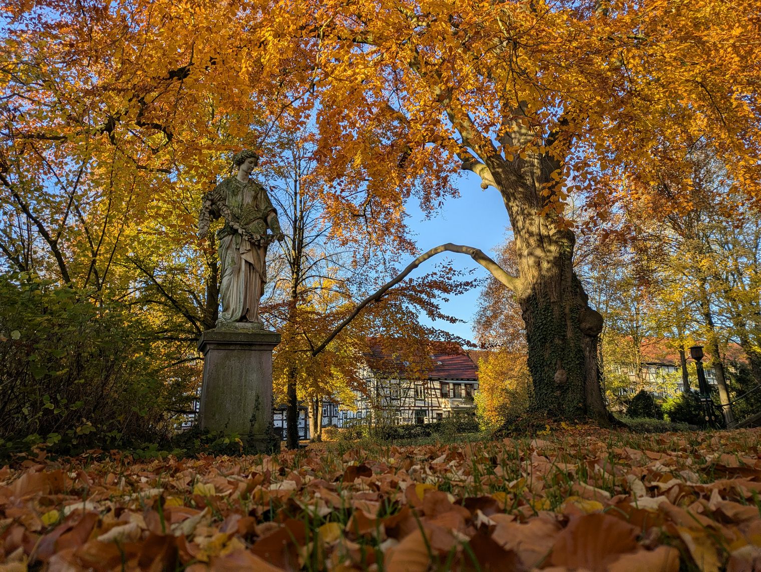 Herbstliche Parkszene mit Statue vor der Stukenbrokvilla, umgeben von buntem Laub und Bäumen.