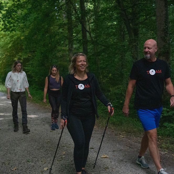 Vier Erwachsene wandern lachend auf einem Waldweg im Grünen beim Nordic Walking in Einbeck.