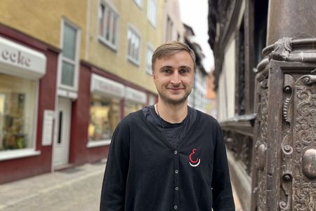 Eine Person steht auf einer Altstadtgasse vor einem reich verzierten historischen Fachwerkhaus.