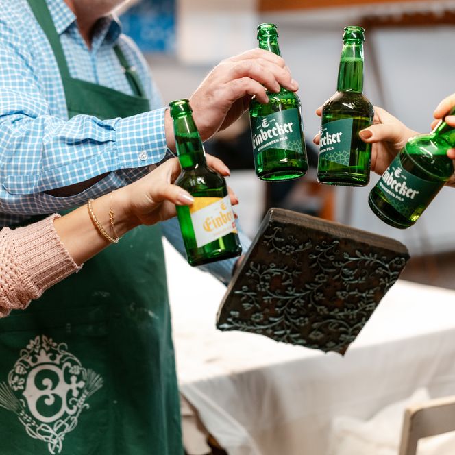 Mehrere Personen stoßen mit Einbecker Bier an und halten eine verzierte Blaudruckplatte.