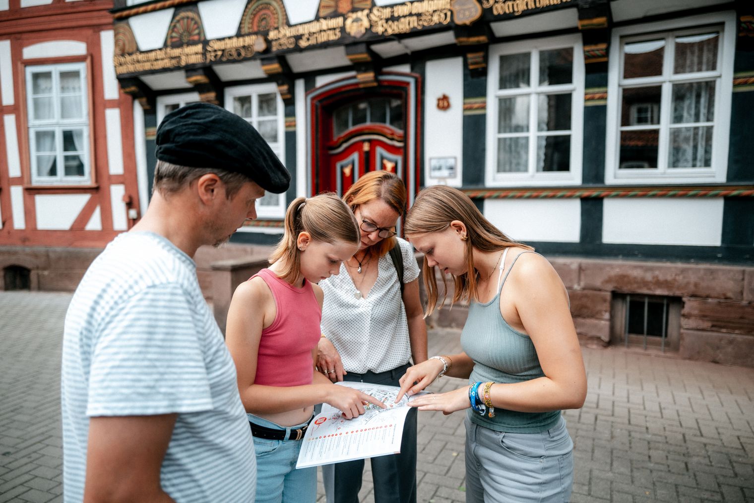 Eine Familie steht vor einem Fachwerkhaus und schaut sich eine Broschüre an.
