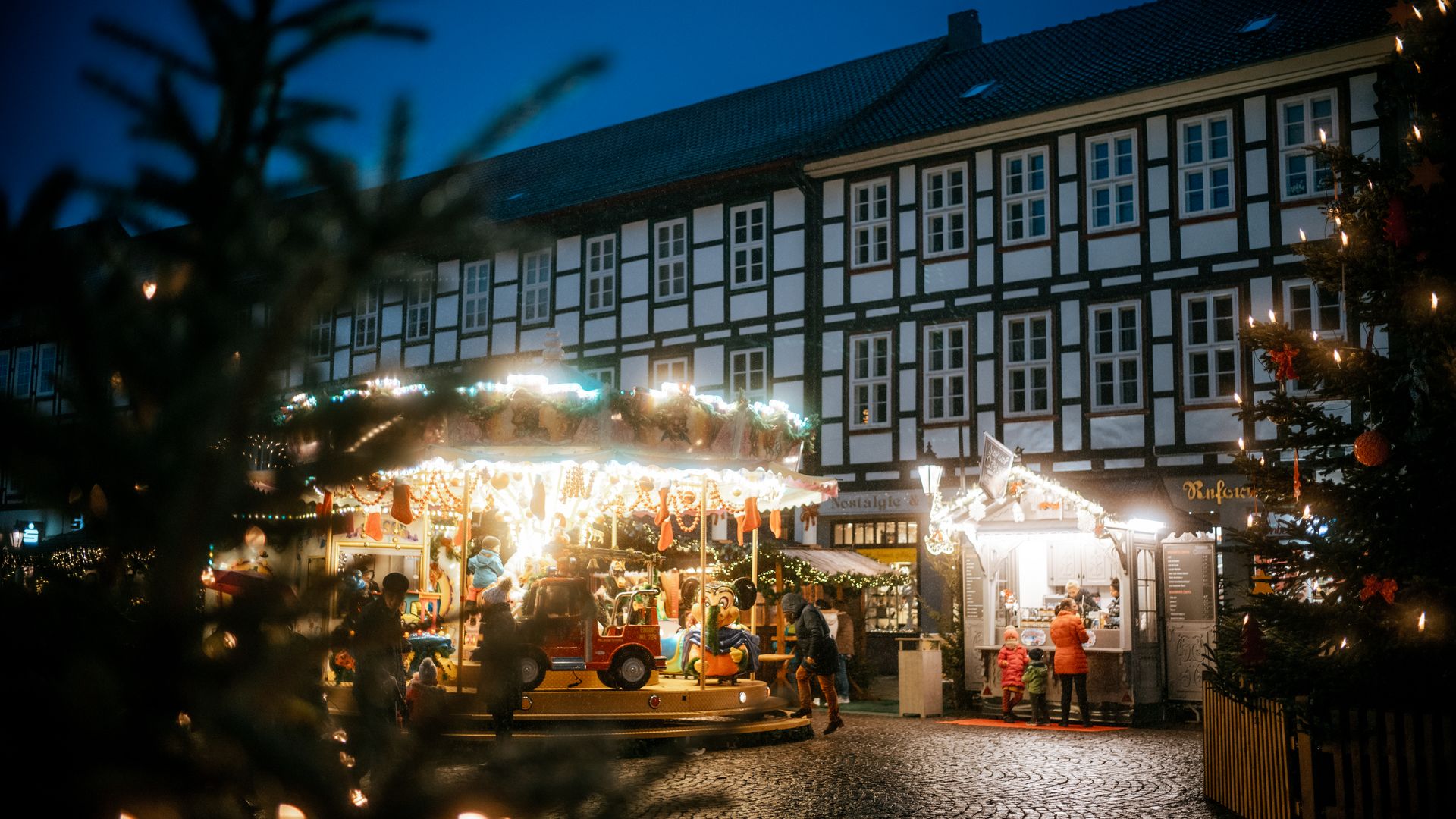 Karussell, Tannenbäume und Stände bei Dämmerung auf dem Einbecker Weihnachtsdorf.