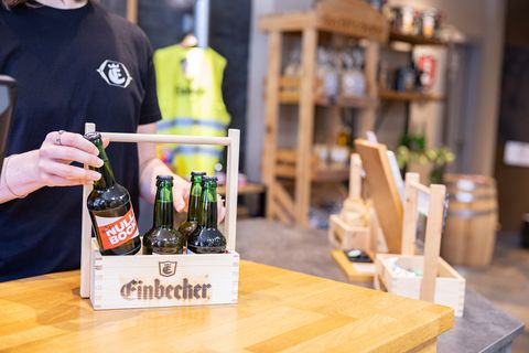 Person stellt eine Bierflasche in einen Einbecker Holz-Sixpack auf dem Tresen im Fan-Shop.