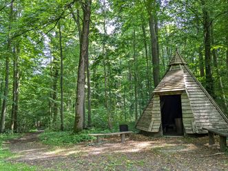 Köhlerhütte zwischen hohen Bäumen im grünen Stadtwald Hube bei Einbeck mit Sitzbänken.