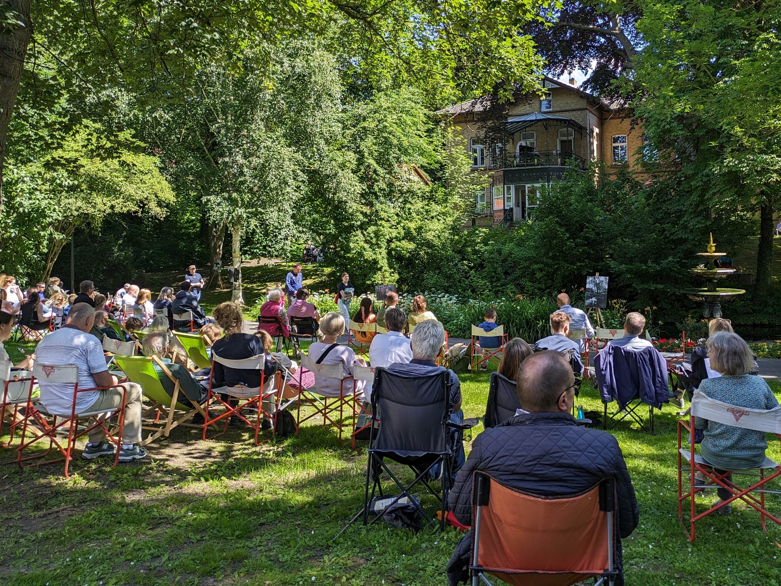 Man sieht Publikum beim Picknick-Konzert im Park, einen Pianisten und historische Kostüme.