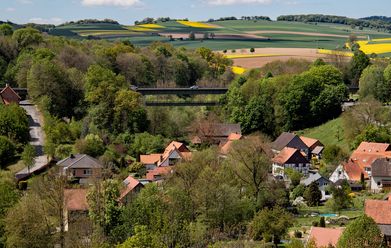Blick über Kuventhal mit der Talbrücke, umgeben von Feldern, Wäldern und roten Hausdächern.