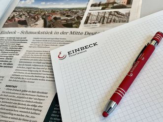 Bildschirm, Stift, Papier und Zeitung auf einem Tisch als Symbole für Öffentlichkeitsarbeit.