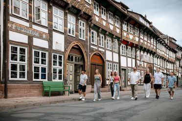 Mehrere Menschen laufen durch eine von Fachwerkhäusern gesäumte Straße.