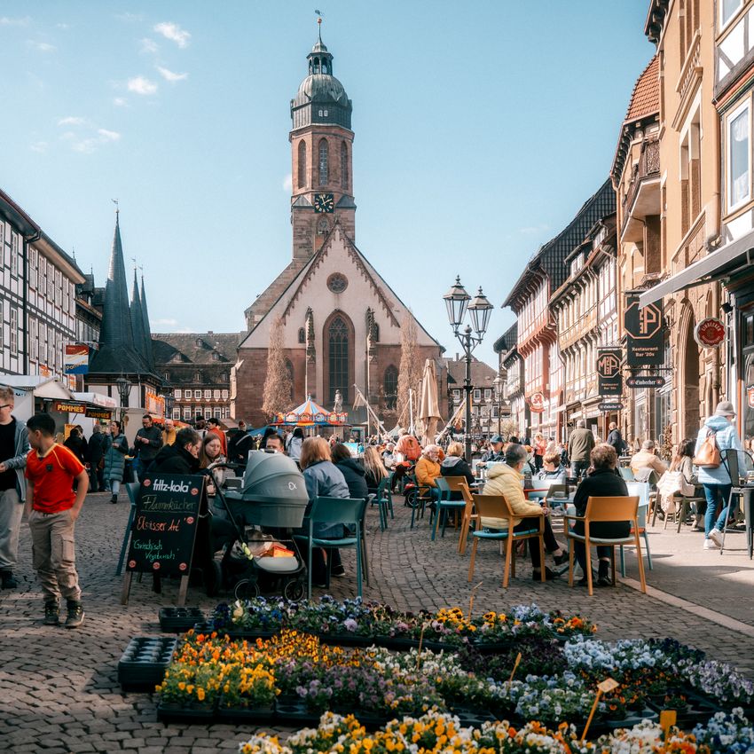 Belebter Frühjahrsmarkt in Einbecks Altstadt mit Ständen, Blumen und Kirche im Hintergrund.