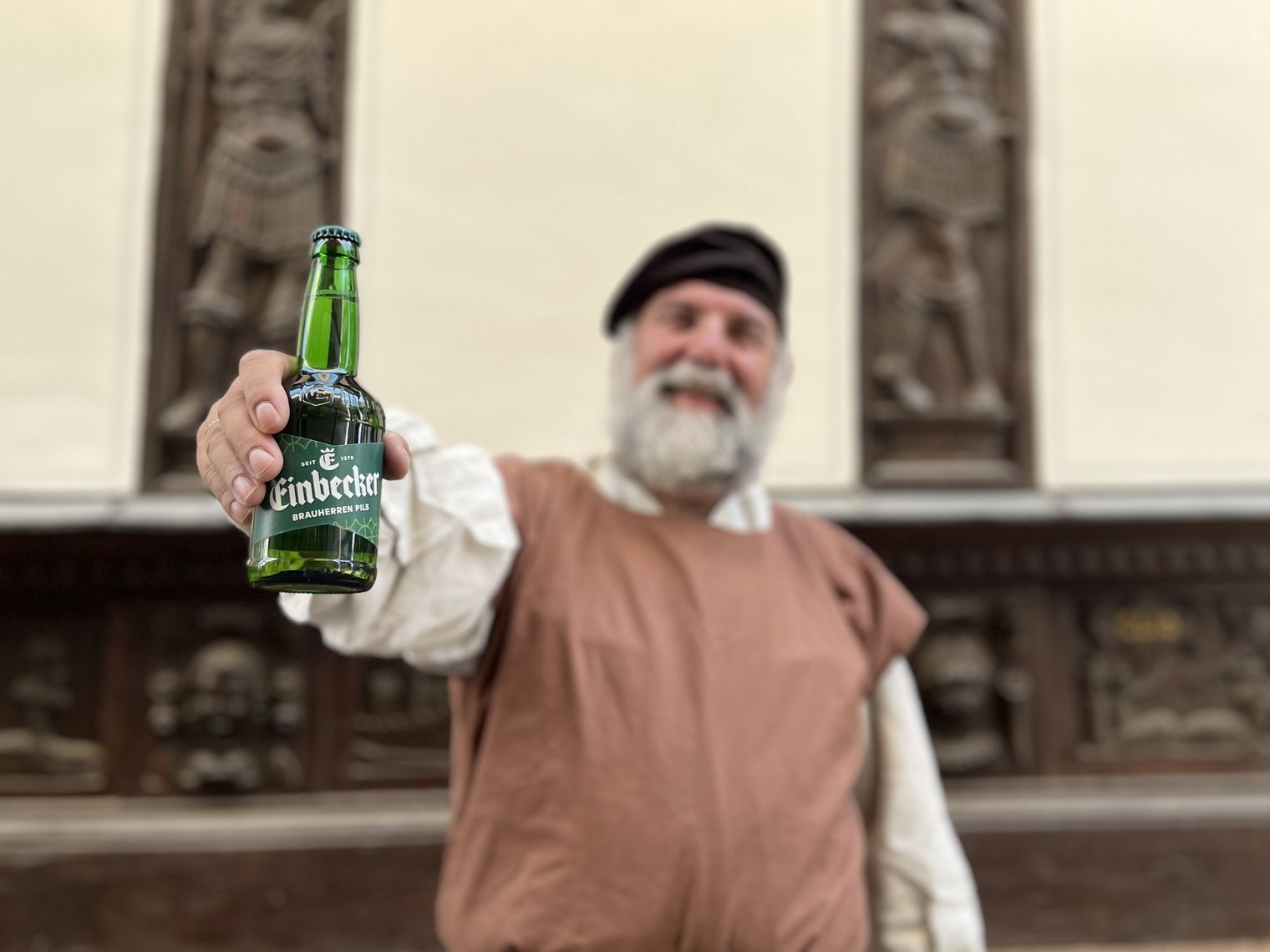 Einbecker Braumeister hält vor einem Fachwerkhaus eine Einbecker Bierflasche in die Kamera