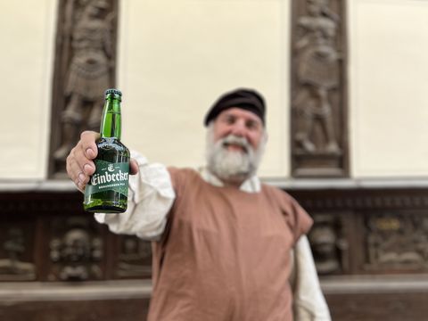 Einbecker Braumeister hält vor einem Fachwerkhaus eine Einbecker Bierflasche in die Kamera
