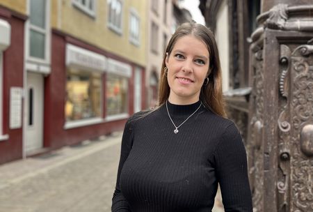 Frau mit schwarzem Pullover steht in historischer Altstadt vor reich verziertem Fachwerkhaus.
