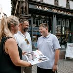 Familie steht mit einer aufgeschlagenen Broschüre vor der Tourist-Information.
