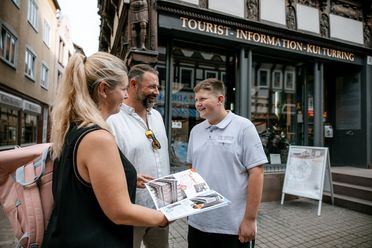 Eine Familie informiert sich vor der Tourist-Information Einbeck mit Stadtplan und lächelt einander zu.