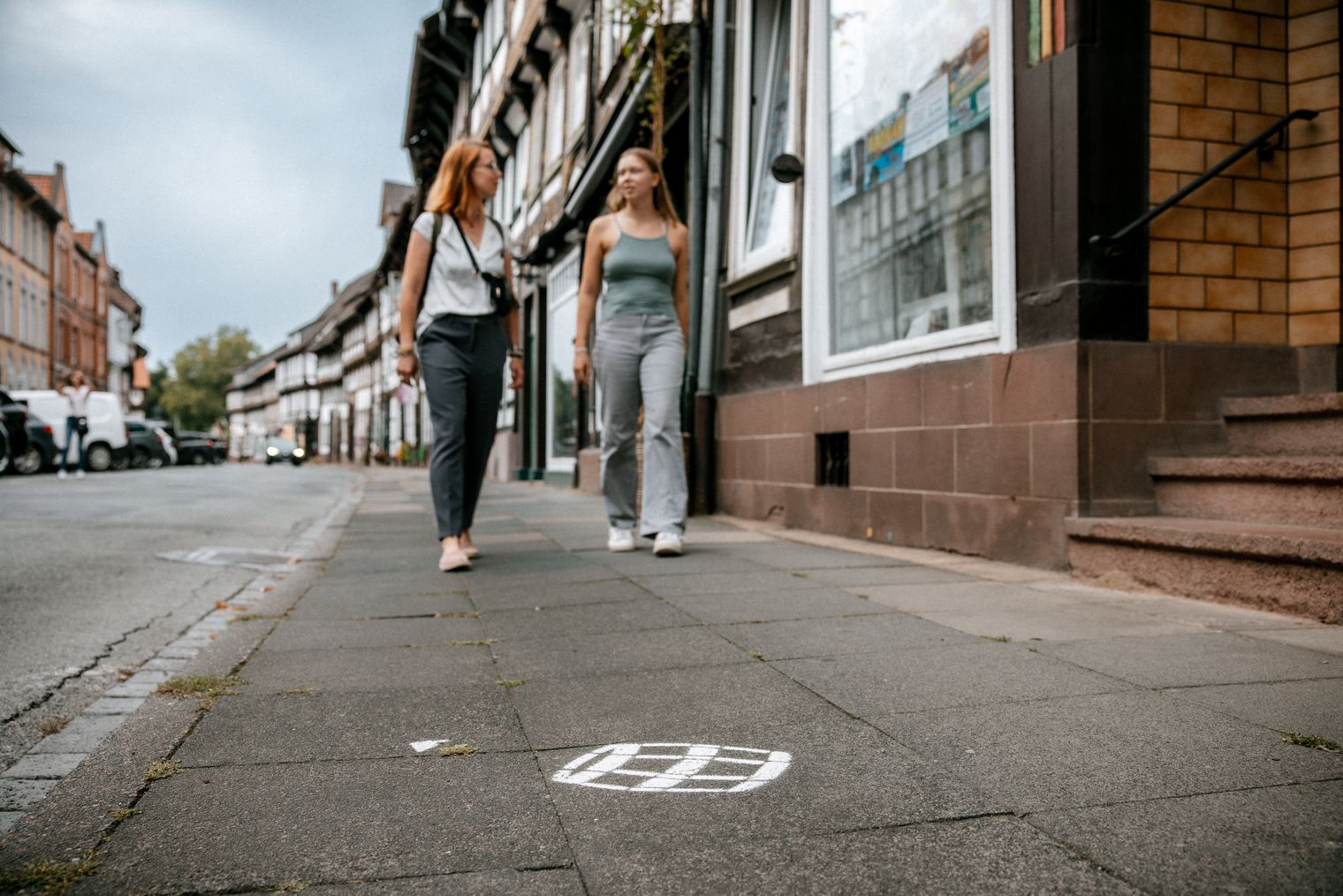 Zwei Personen gehen auf dem Bürgersteig in der Einbecker Innenstadt, auf dem Boden aufgemalt ein Faß vom Bierpfad.