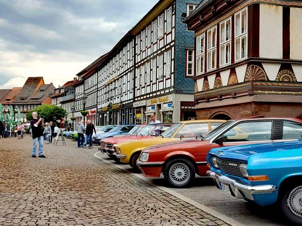 Zu sehen sind Opel-Oldtimer auf dem Einbecker Marktplatz mit herrlicher Fachwerkkulisse bei leicht bewölktem Himmel.