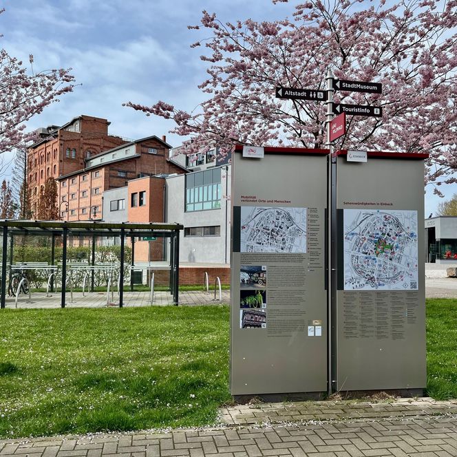 Die PS.Pfad Stele in Einbeck mit Wegweisern unter Kirschblüten vor dem PS.SPEICHER.