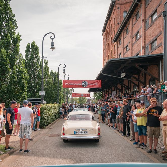 Menschen stehen links und rechts der Fahrbahn am PS.SPEICHER, um die Oldtimer zu bewundern.