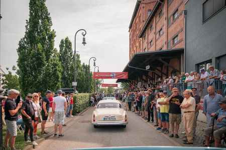 Menschen stehen links und rechts der Fahrbahn am PS.SPEICHER, um die Oldtimer zu bewundern.